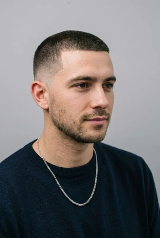 A professional photo of a man with an oval face shape, featuring a high-quality buzz cut with a defined taper on the sides and back, suitable for a male hairstyle guide.